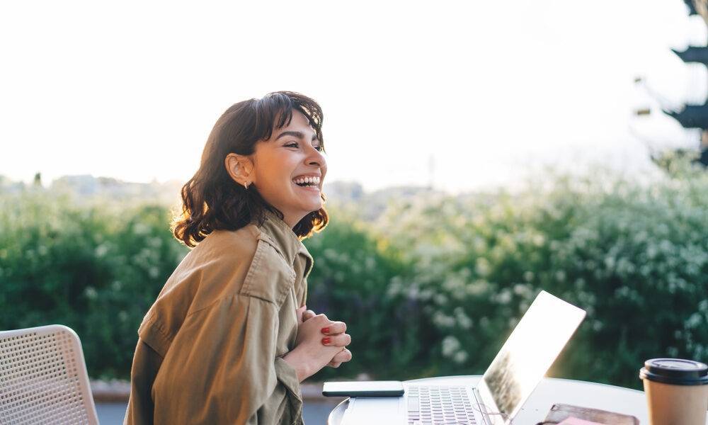 Remote Work Tips: A remote work lady sitting with her laptop in a remote work settings. She looks very happy.