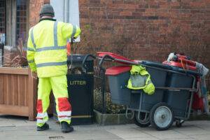Unskilled Jobs You Can Do in the UK: street sweeper collecting litter with street barrow in reflective gear and placing it in bin
