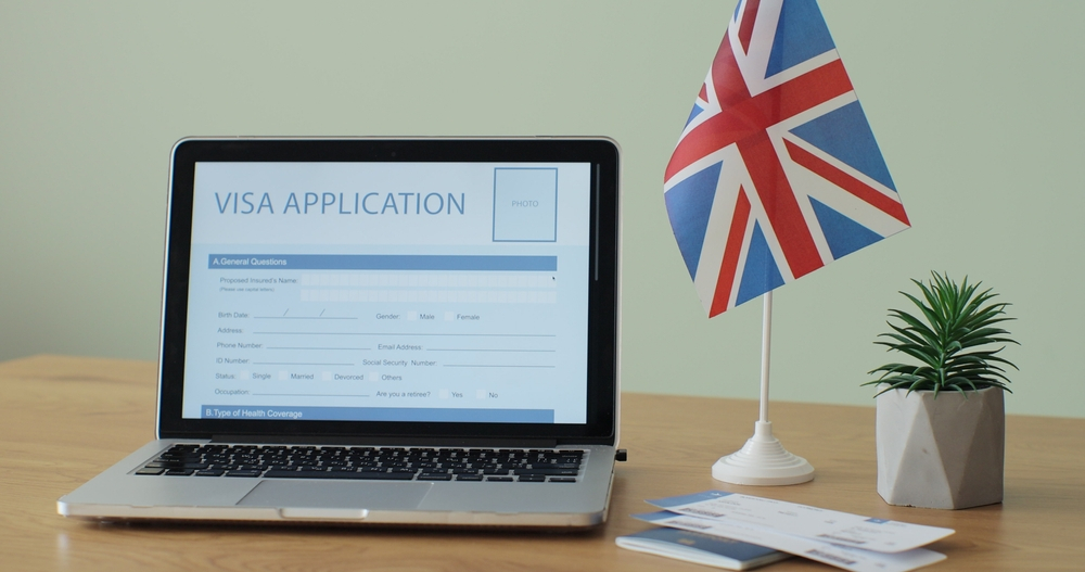 Things to Avoid During the UK Visa Application Process: A picture showing a laptop with visa application form displaying on it, placed on the table with UK flag.