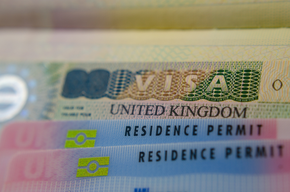 The 8 Worst Mistakes That Can Derail Your UK Employment Dreams: United Kingdom BRP (Biometrical Residence Permit) cards for Tier 2 work visas placed on top of UK VISA stickers in the passport. Close up photo. 