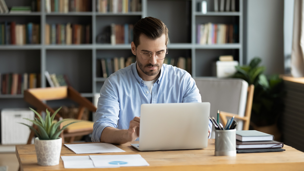 The Ultimate Guide to Setting Up a Productive Home Office: Picture of a focused freelancer at his workplace desk in the home office cozy room working on a laptop.