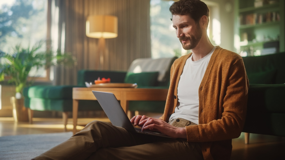 Worst Remote Work Habits That Kill Productivity: Handsome Happy Man Using Laptop at Home for Remote Work.