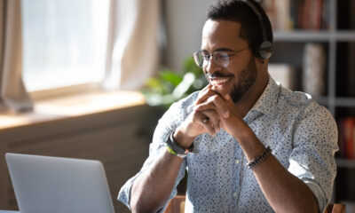Secrets to Landing Your Dream Remote Job: Happy freelancer in glasses wearing headphones, enjoying watching educational webinar on laptop.