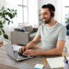 Things to Know Before Accepting a Remote Job Offer: Remote job, technology and people concept - happy smiling man with headset and laptop computer having video conference at home office.