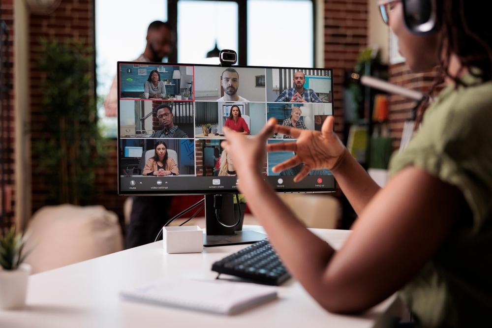 Secrets to Successfully Collaborating with a Remote Team: Picture of a startup employee working from home gesturing in video conference with colleagues at the desk.