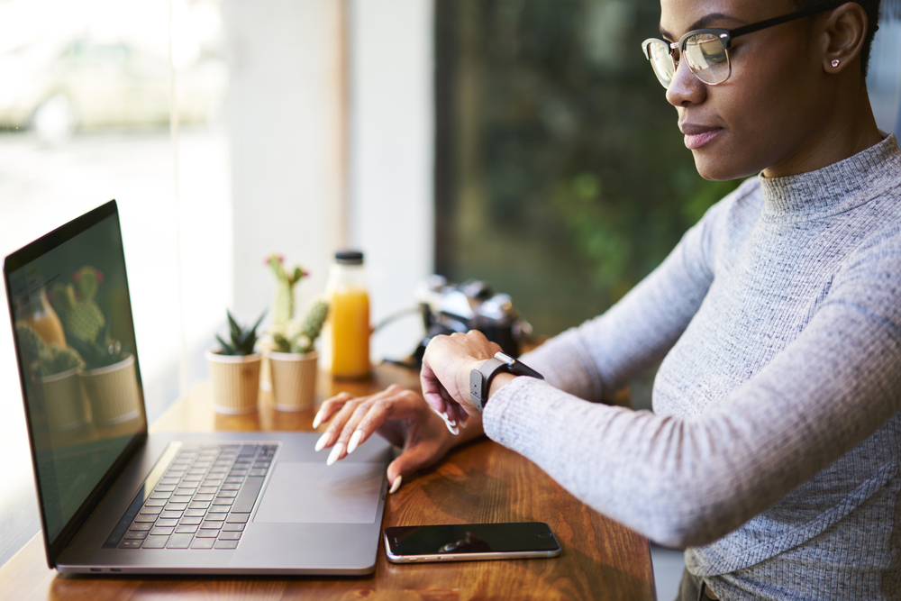Things to Know Before Working Remotely from a Different Time Zone: Picture of a female in trendy eyewear checking time while waiting for payment confirmation making transaction online.