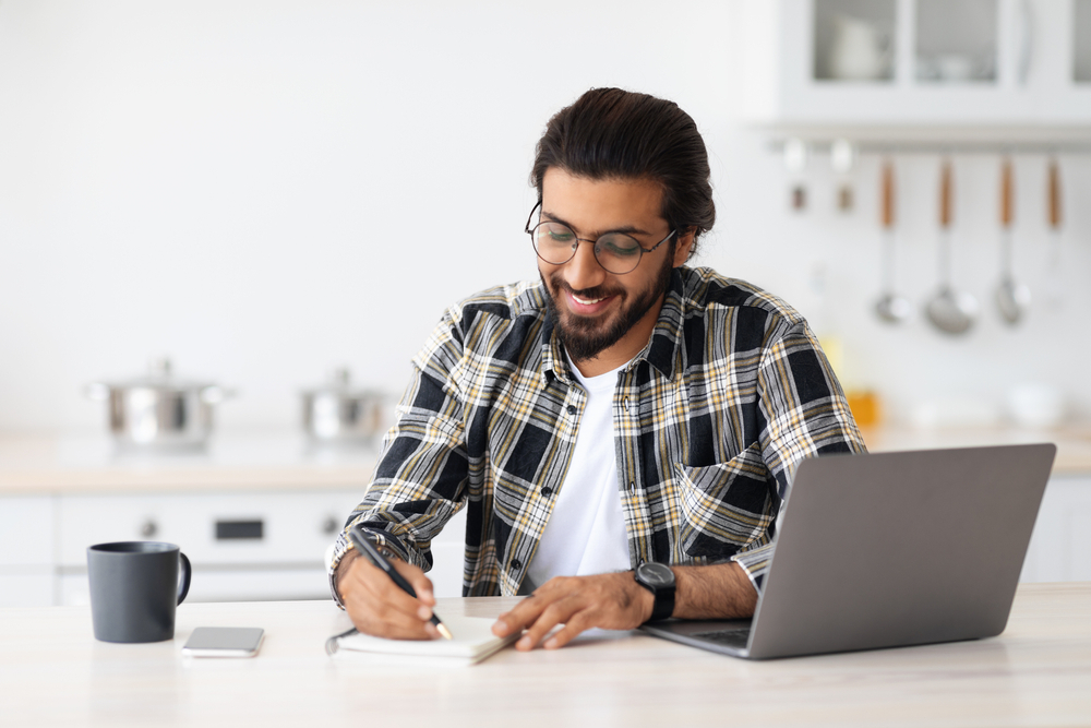 Remote Work vs. Office Work: Picture of male freelancer with glasses working on laptop from home.