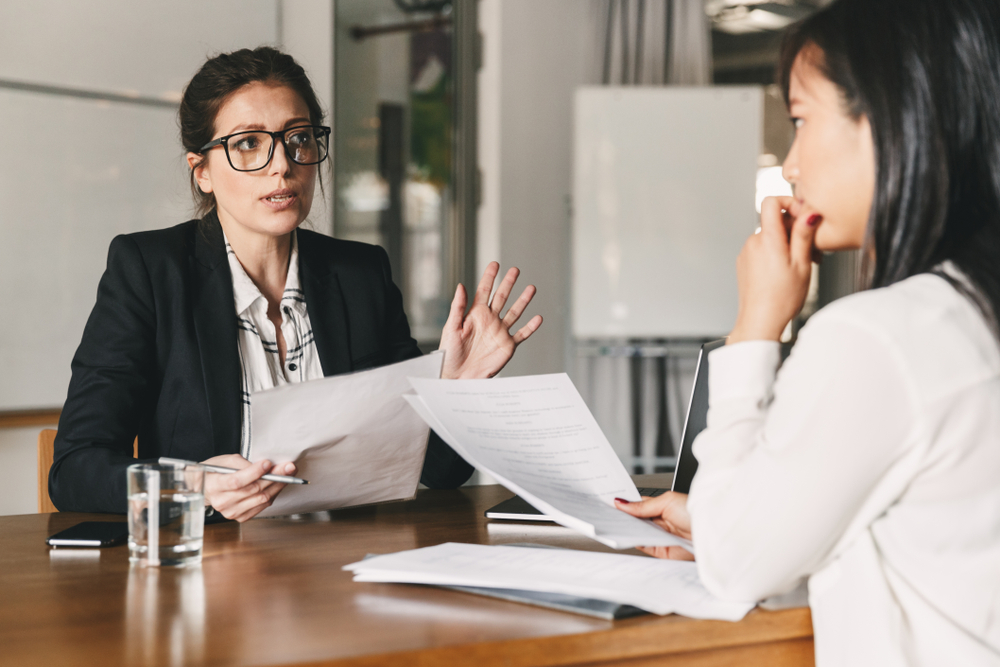 What Not to Say During a Canada Work Permit Interview: Photo of woman holding resume and negotiating with female candidate during job interview. 