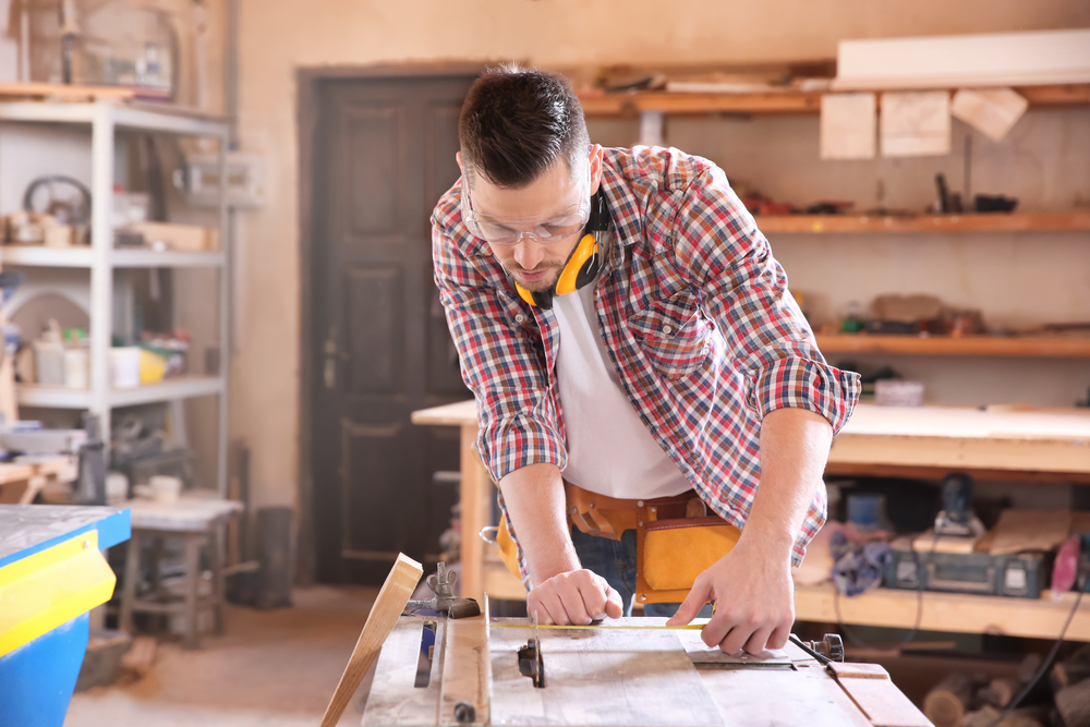 Self-Employment vs Employment in the UK: Picture of a carpenter taking measurements for working with wooden plank in shop 