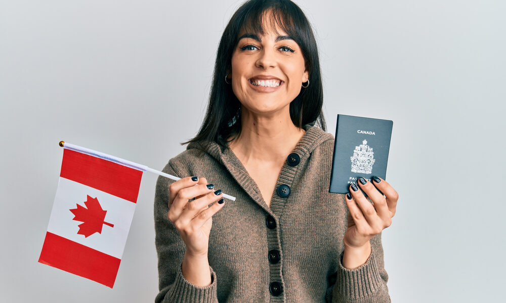 Skilled Worker Visa vs Study Permit: Picture of a young woman holding a canada flag and passport smiling with a happy and cool smile on face.