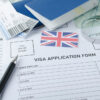 In-Person vs Virtual UK Visa Appointments: Visa application form, passports, tickets,English flag, magnifying glass on the world map.