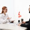 Canada Work Visa Pitfalls: : Smiling woman having interview with embassy worker in office