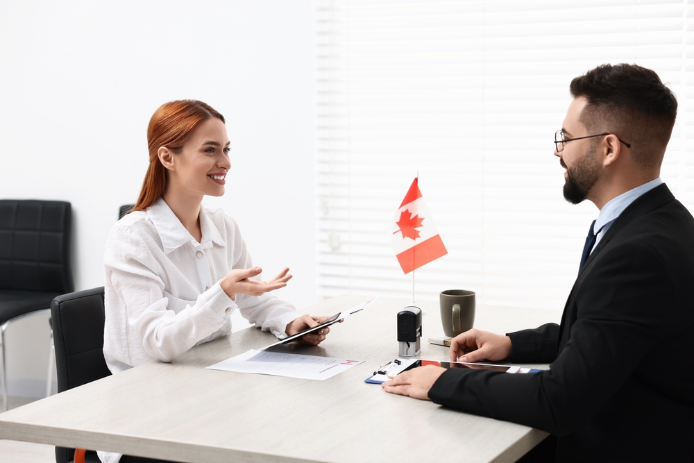 Canada Work Visa Pitfalls: : Smiling woman having interview with embassy worker in office