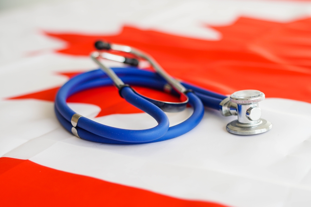 Travel Insurance for Canada vs Health Insurance for Canada: Medical stethoscope on a Canada flag. Canadian health care system, insurance. 