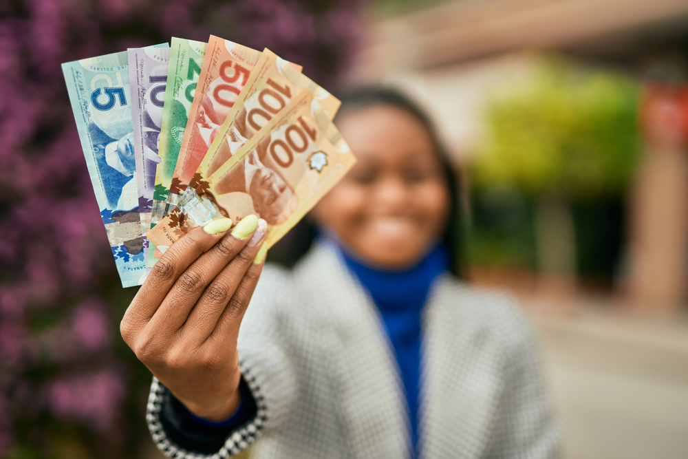 How Salary Negotiation in Canada Works: Young african american businesswoman smiling happy holding canadian dollars at the city.
