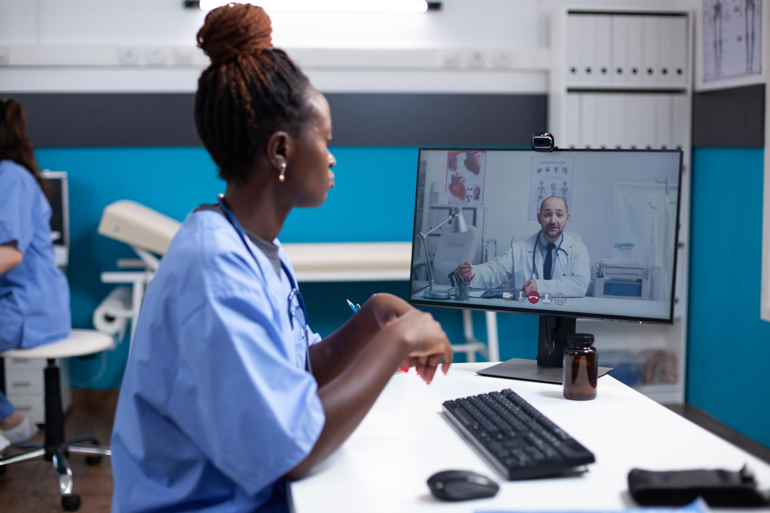 Remote Jobs for Nurses: African american nurse at clinic desk listening to general practitioner collegue doctor during video conferencing. Medical team in telemedicine call at busy modern hospital office 